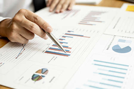 A close-up of a financial businessman holding a pen and pointing at the information sheet on his desk, reading the company's financials to make a financial plan. Financial concept.の写真素材