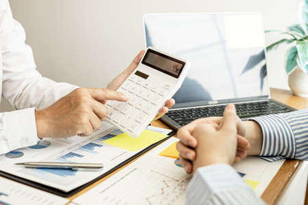 A business man using a calculator to check company financial information Together with business partners, they are having a brainstorming meeting planning to grow the company. Financial concept.の写真素材