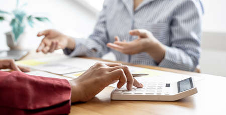 A close-up of the sales manager pressing the white calculator, she is examining the sales figures with management to summarize the monthly results and joint planning. Sales management concept.の写真素材