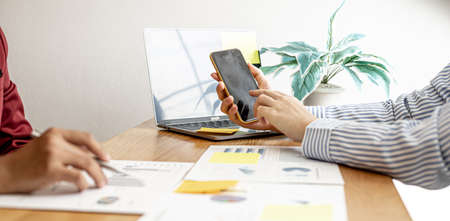Sales are working together to summarize monthly sales to bring in a meeting with executives, female employees using smartphones to view sales data. Sales management concept.の写真素材