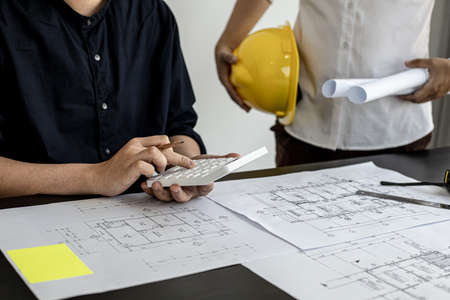 The architect was pressing the white calculator and there was an engineer standing there holding the floor plan. They are examining the draft blueprint for the designed building. Construction and interior ideas.の写真素材