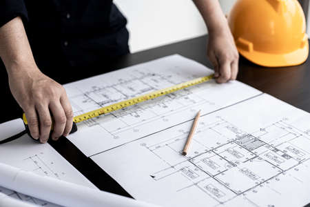 An engineer is using a tape measure to measure the plans of the house that he designs, the drafts...