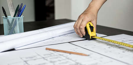 An engineer is using a tape measure to measure the plans of the house that he designs, the drafts the house drawings to build the correct standard. Engineer concept.の写真素材