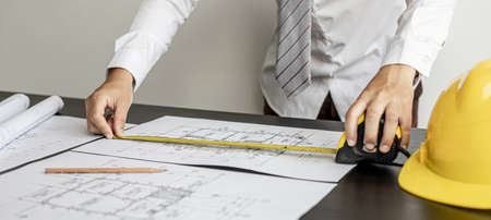 An engineer is using a tape measure to measure the plans of the house that he designs, the drafts the house drawings to build the correct standard. Engineer concept.の写真素材