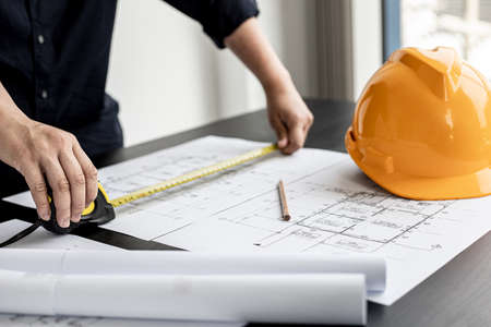 An engineer is using a tape measure to measure the plans of the house that he designs, the drafts the house drawings to build the correct standard. Engineer concept.の写真素材