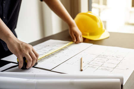 An engineer is using a tape measure to measure the plans of the house that he designs, the drafts the house drawings to build the correct standard. Engineer concept.の写真素材