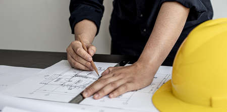 An architect, a home design engineer, is drafting a house plan for a client in his office. He is writing a house plan based on the needs of his clients. House building and interior ideas.の写真素材