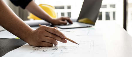A close-up, an architect, a house designer holding a pencil, pointing to a house plan to examine the design plan before discussing the details with the client. Interior design and decoration ideas.の写真素材