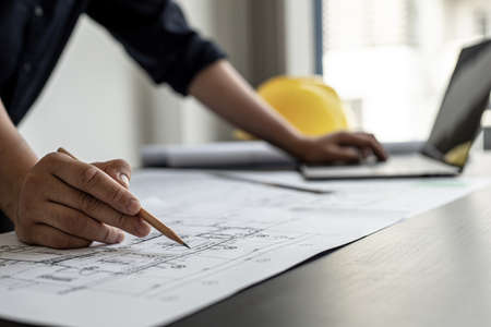 A close-up, an architect, a house designer holding a pencil, pointing to a house plan to examine the design plan before discussing the details with the client. Interior design and decoration ideas.の写真素材