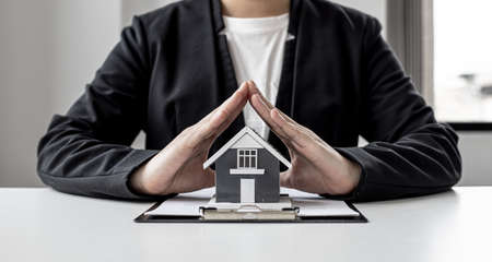 A home insurance salesman is using his hand to make a triangle pose on the small gray home model as a sign of protection. Concept of home insurance.の写真素材