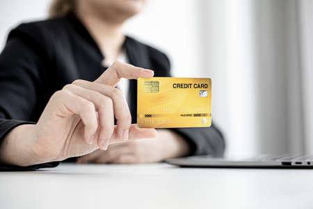 A business woman holds a credit card to make payments on the website where she is shopping online. Concept of using credit cards to pay for goods and services on online websites.の写真素材