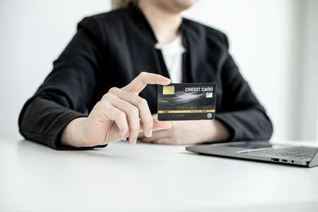 A business woman holds a credit card to make payments on the website where she is shopping online. Concept of using credit cards to pay for goods and services on online websites.の写真素材
