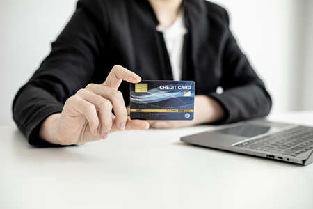 A business woman holds a credit card to make payments on the website where she is shopping online. Concept of using credit cards to pay for goods and services on online websites.の写真素材