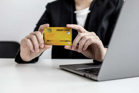 A business woman holds a credit card to make payments on the website where she is shopping online. Concept of using credit cards to pay for goods and services on online websites.の写真素材