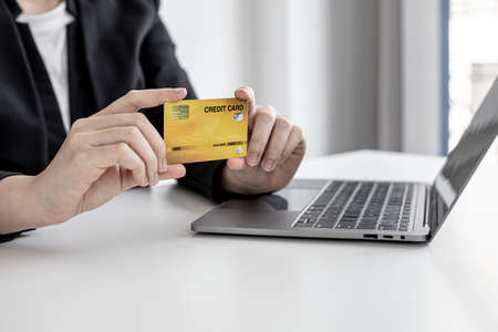 A business woman holds a credit card to make payments on the website where she is shopping online. Concept of using credit cards to pay for goods and services on online websites.の写真素材