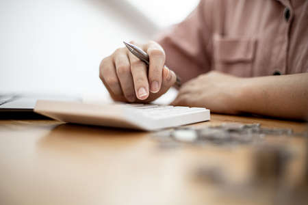 A woman is using a calculator to calculate money, she is doing an income and expenditure account to divide the money into savings and to buy funds to grow. Concept of saving money and investing.の写真素材