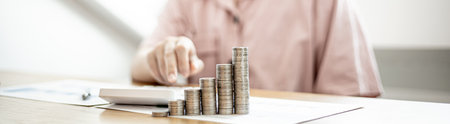 Stacked coins on a woman's desk, she was doing income and expenditure accounts to divide the money into savings and to buy funds to grow. Concept of saving money and investing.の写真素材