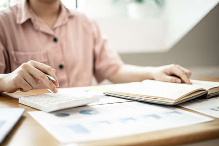 A woman is using a calculator to calculate money, she is doing an income and expenditure account to divide the money into savings and to buy funds to grow. Concept of saving money and investing.の写真素材