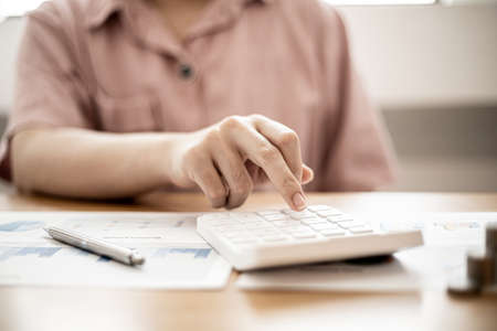 A woman is using a calculator to calculate money, she is doing an income and expenditure account to divide the money into savings and to buy funds to grow. Concept of saving money and investing.の写真素材