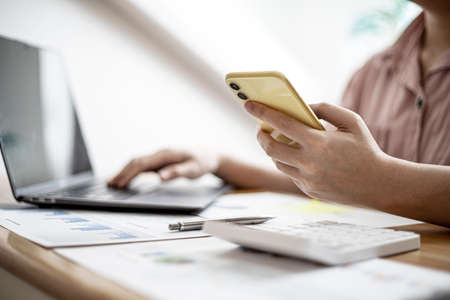 The businesswoman is using a smartphone to communicate with the company's finance department to...