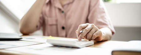 Businesswoman is using a calculator to check the numbers on a company financial document during a meeting with shareholders, corporate finance documents showing a bar graph format. Financial concept.の写真素材