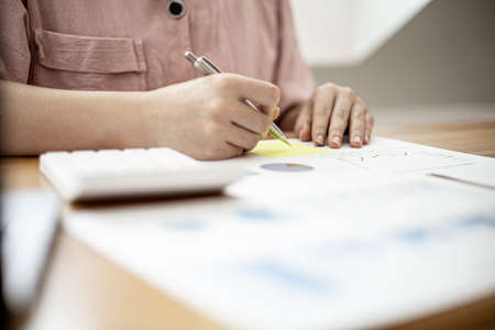 A businesswoman is taking notes on a note on a company financial information sheet for a meeting with a partner, taking important notes on a note on the main meeting papers. Financial concept.の写真素材