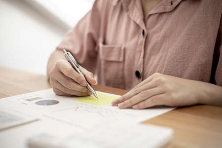 A businesswoman is taking notes on a note on a company financial information sheet for a meeting with a partner, taking important notes on a note on the main meeting papers. Financial concept.の写真素材