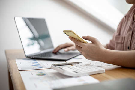 The businesswoman is using a smartphone to communicate with the company's finance department to verify the accuracy of information from the document producer before attending a meeting with a partner.の写真素材