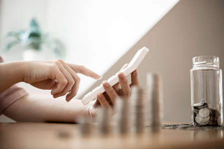 A woman is using a calculator to calculate money, she is doing an income and expenditure account to divide the money into savings and to buy funds to grow. Concept of saving money and investing.の写真素材
