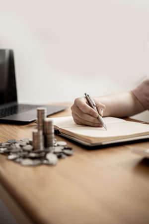 A woman is writing her income and expenses in her book, she keeps a monthly account to plan her savings and invest the money. Concept of saving money and investing it to grow money.の写真素材