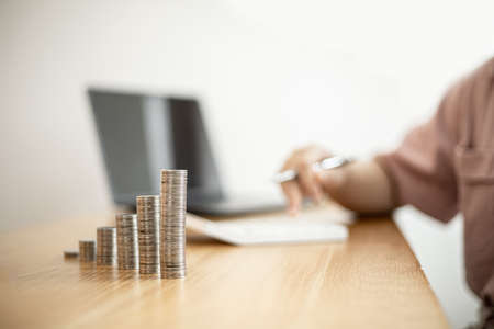 Stacked coins on a woman's desk, she was doing income and expenditure accounts to divide the money into savings and to buy funds to grow. Concept of saving money and investing.の写真素材