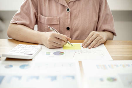 A businesswoman is taking notes on a note on a company financial information sheet for a meeting with a partner, taking important notes on a note on the main meeting papers. Financial concept.の写真素材