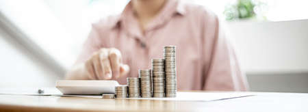 Stacked coins on a woman's desk, she was doing income and expenditure accounts to divide the money into savings and to buy funds to grow. Concept of saving money and investing.の写真素材