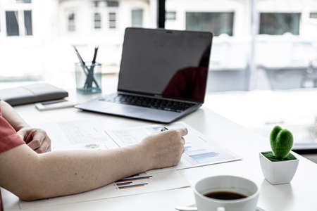 A corporate finance employee is pointing at the document with a pen to verify the accuracy of the...