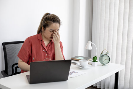 A business woman was tired from work for a long time, she was taking a break to relax from work, she sat in her office and spent a long time using the laptop causing fatigue. Office Syndrome Concept.の写真素材