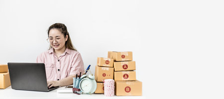 The start-up owner is chatting and responding to customers through the company's online sales page, she is taking orders and preparing packages for delivery by a private shipping company. copy spaceの写真素材
