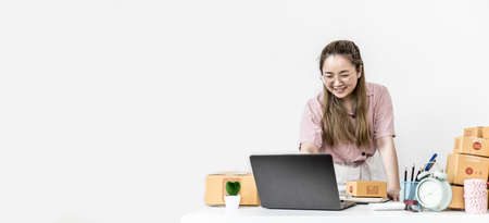 The start-up owner is chatting and responding to customers through the company's online sales page, she is taking orders and preparing packages for delivery by a private shipping company. copy spaceの写真素材