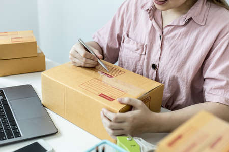 Online trading vendors are writing customer shipping address information, her pack of orders, ordering through her shop website and sending goods through private transportation. Online sales concepts.の写真素材