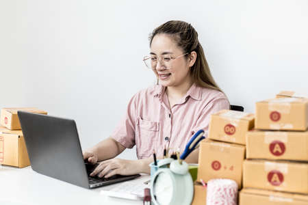 The start-up owner is chatting and responding to customers through the company's online sales page, she is taking orders and preparing packages for delivery by a private shipping company. copy spaceの写真素材