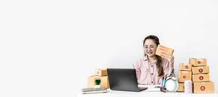 An online store owner holding a parcel showing a live camera on the page, she runs a popular online...