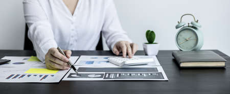 Close-up of a business woman holding a pen and pointing at a financial data sheet and pressing a calculator, she is checking monthly financial documents from the finance department. Financial concept.の写真素材