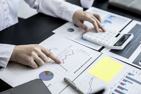 A businesswoman is pressing a white calculator to calculate the financial figures on the company's quarterly financial summary, prepared from the Finance Department. Company financial concept.の写真素材