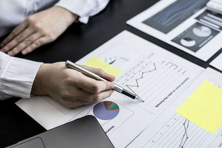 A close-up businesswoman holding a pen and pointing at a company financial statement, she is...