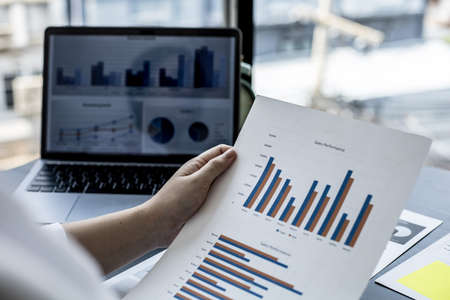 A woman uses a laptop and presses a white calculator, she is a company auditor, she checks documents from the laptop and calculates the numbers for accuracy. Financial audit conceptの写真素材