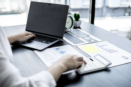 A woman uses a laptop and presses a white calculator, she is a company auditor, she checks documents...
