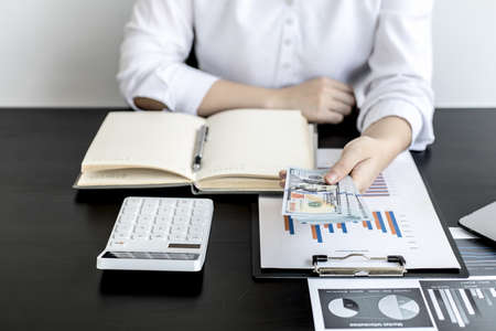 A woman pressing a white calculator and holding money, she is keeping a personal account by recording income and expenses in a notebook, personal bookkeeping to plan and manage money spending.の写真素材