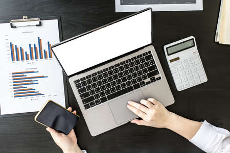 Top view woman holding a smartphone and using a laptop uses a smartphone. Chat with friends through instant messaging to discuss business together and use your laptop to find information on the web.の写真素材