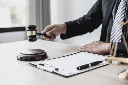 A lawyer or legal advisor holding a small hammer for a judge's table in court is about to pound on...