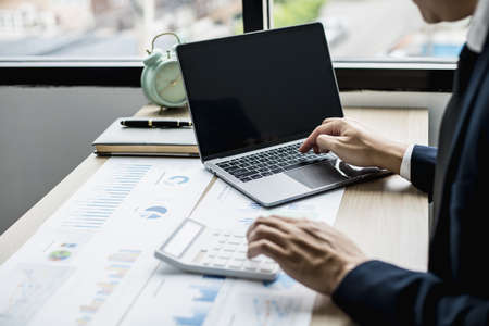 Man using laptop and pressing calculator, business man sitting in private office at his company, he runs a startup company, he's a young man starting a business. Management concept of startup company.の写真素材