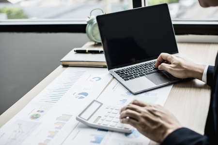 Man using laptop and pressing calculator, business man sitting in private office at his company, he runs a startup company, he's a young man starting a business. Management concept of startup company.の写真素材